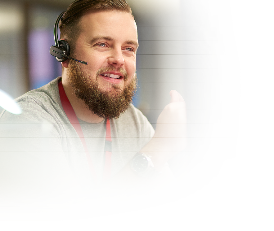 a call centre phone operative in his mid 30s chats on the phone at his desk   He is explaining something to the person on the phone in a friendly manner   behind him a defocussed office interior can be seen   This could be a call centre or an office worker chatting to a customer  