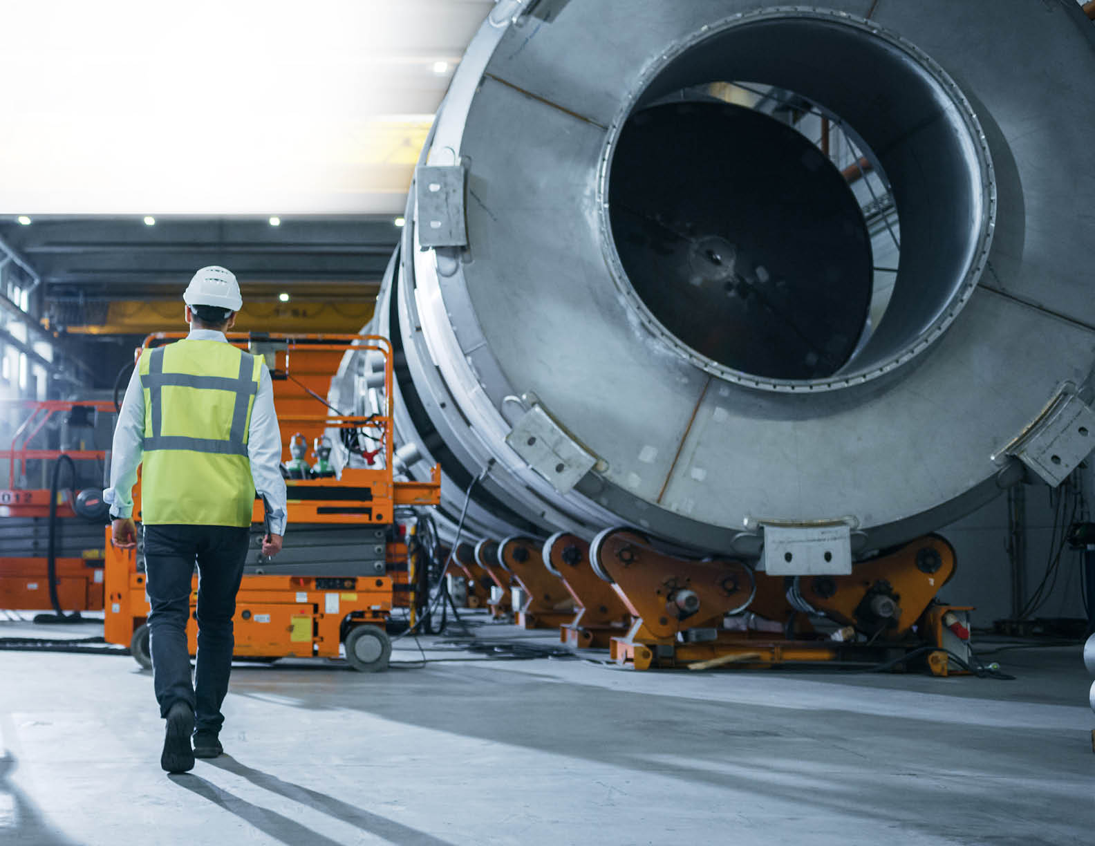 Following Shot of Heavy Industry Engineers Walking Through Manufacturing Factory  In the Background Professionals Working on Construction of Oil, Gas and Fuel Pipeline Transportation Products